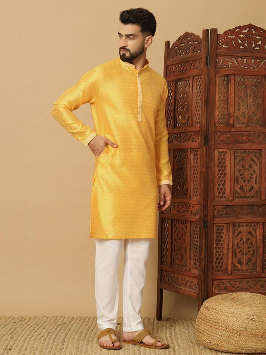 Man wearing a yellow kurta with white pants standing in front of a wooden carved screen.