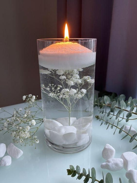 Candle in a glass container with flowers and water on a table