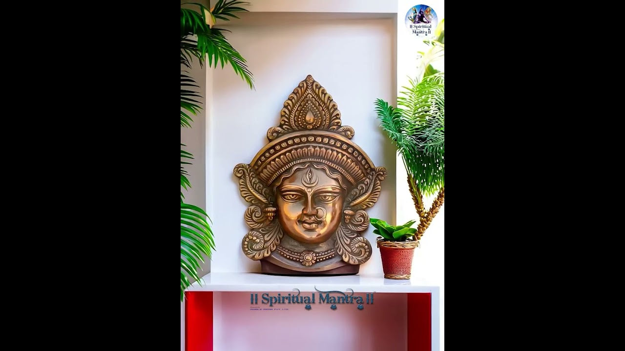 Decorative wall art of a face with spiritual design on a white shelf with plants.