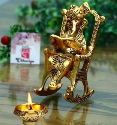 Gold-colored Ganesha statue on a rocking chair with a lit candle in the foreground.