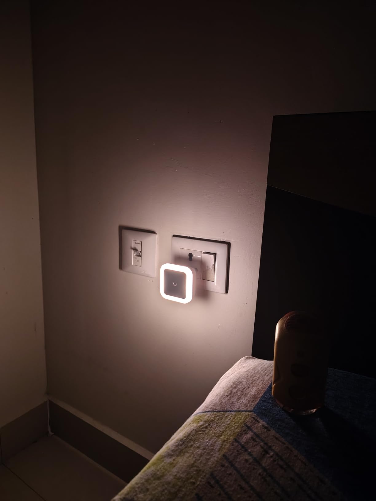 Square wall light fixture on a dark wall next to a bed