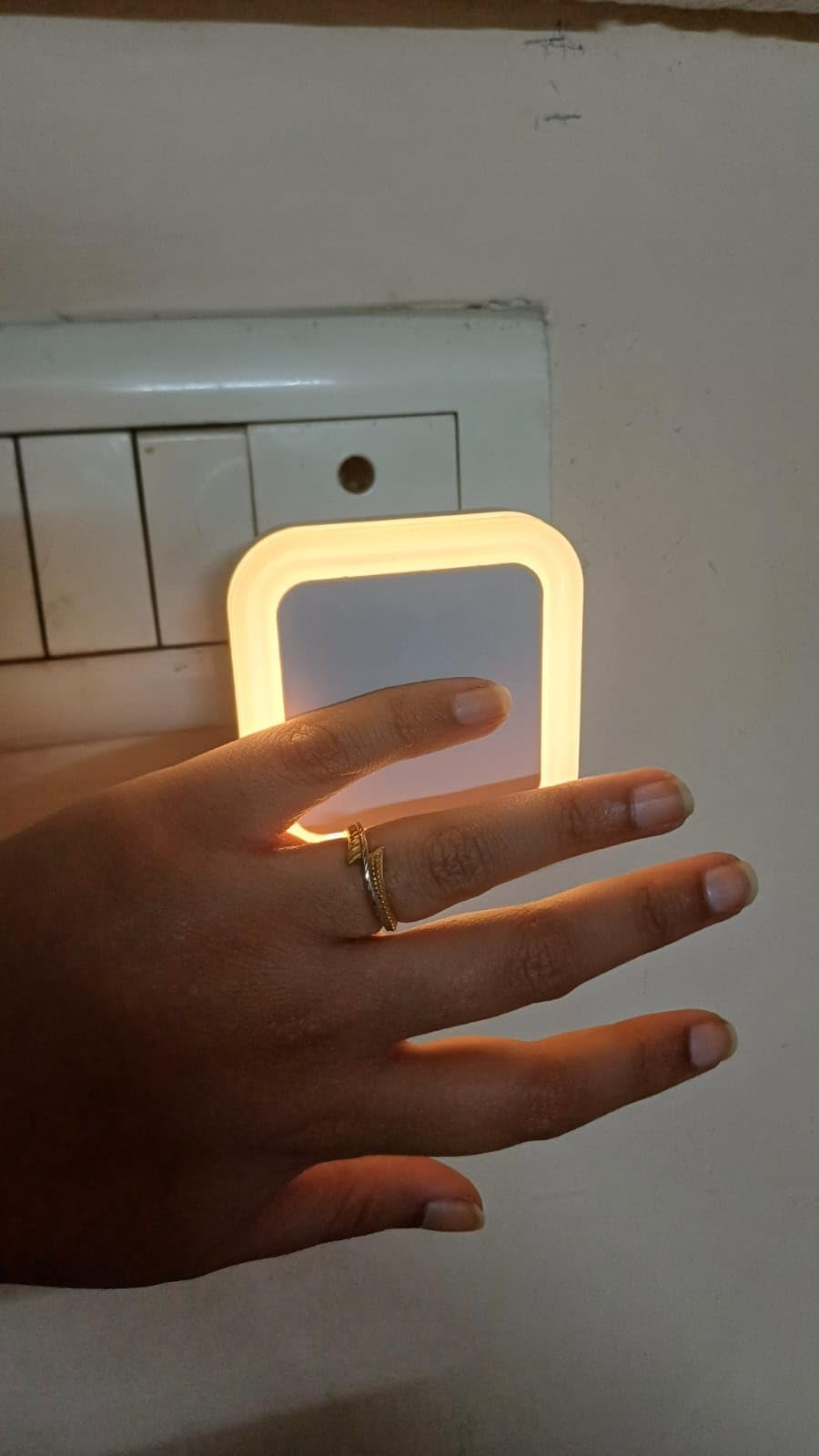 Hand wearing a gold ring with a lighted rectangular object on a plain background