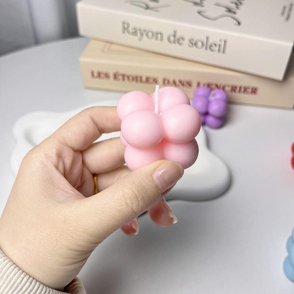 Hand holding a pink bubble-shaped candle with books in the background