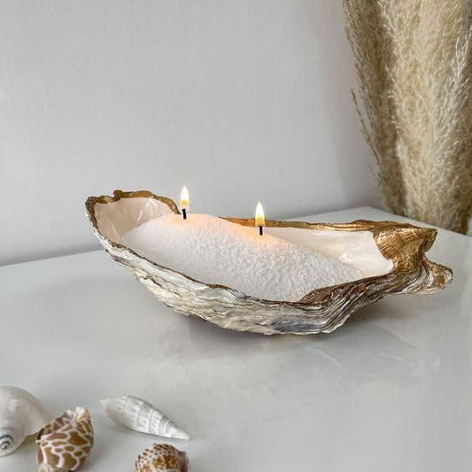 Candle in an oyster shell on a white surface with seashells in the background