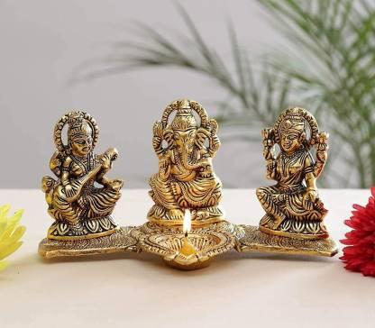Three brass神像 statues on a white surface with a blurred green plant background