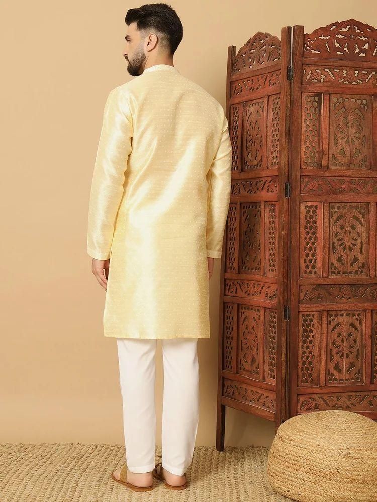 Man wearing a light yellow kurta with white pants standing in front of a wooden carved screen.