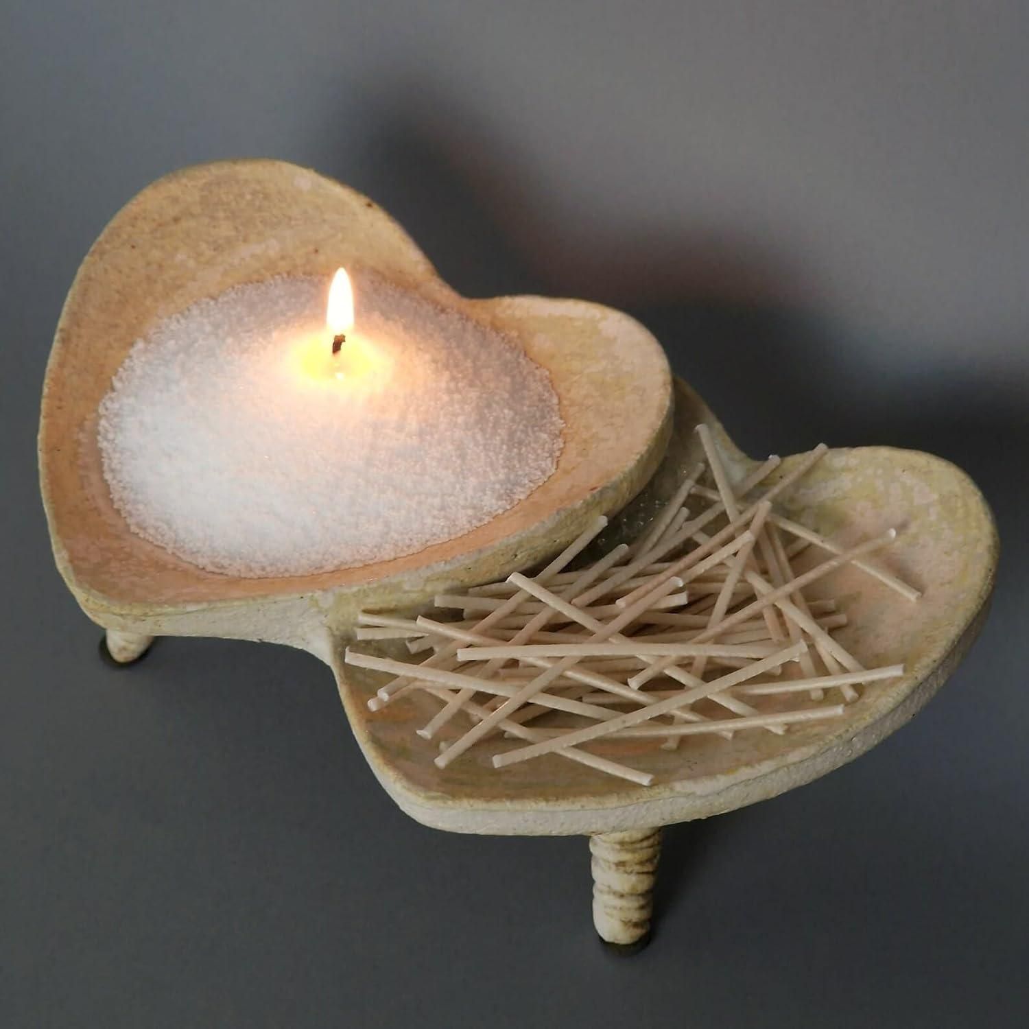 Heart-shaped candle holder with a lit candle and matches on a dark background