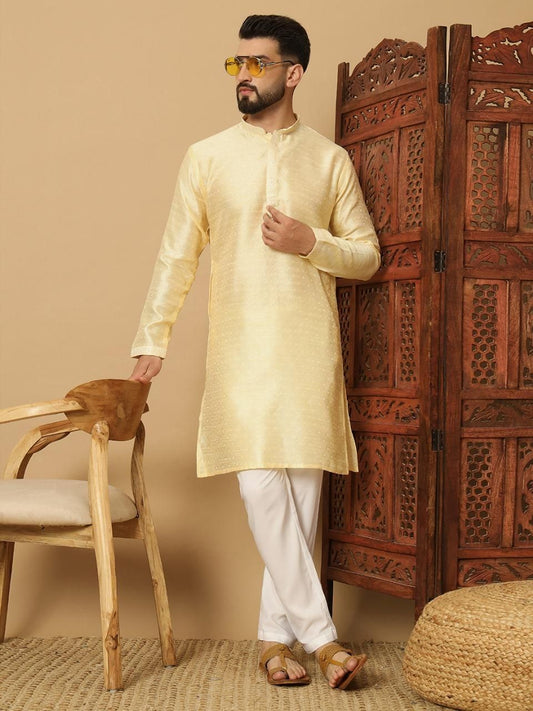 Man wearing a light yellow kurta with white pants in a room with wooden furniture.
