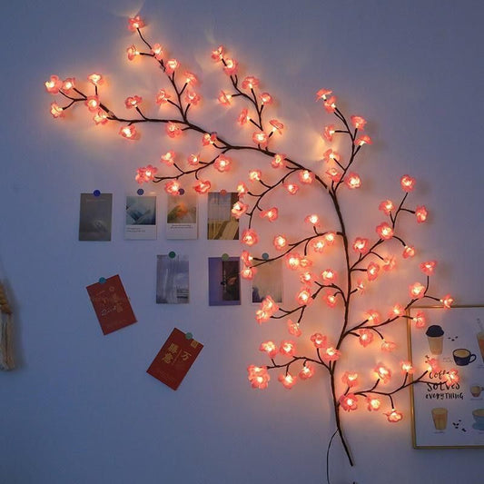 Decorative LED branch with pink lights on a wall with pinned photos and notes.