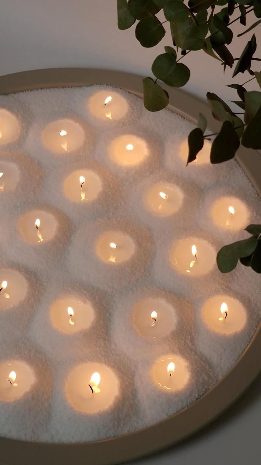 Circular arrangement of lit candles in a white foam block with a plant in the corner.