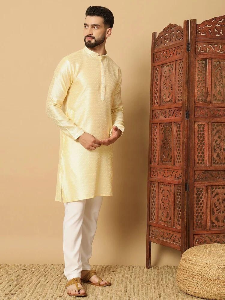 Man wearing a light yellow kurta with white pants standing next to a wooden carved screen.