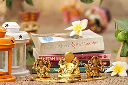Three gold-colored deity statues on a table with books and decorative items in the background.