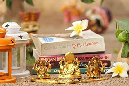 Three gold-colored deity statues on a table with books and decorative items in the background.