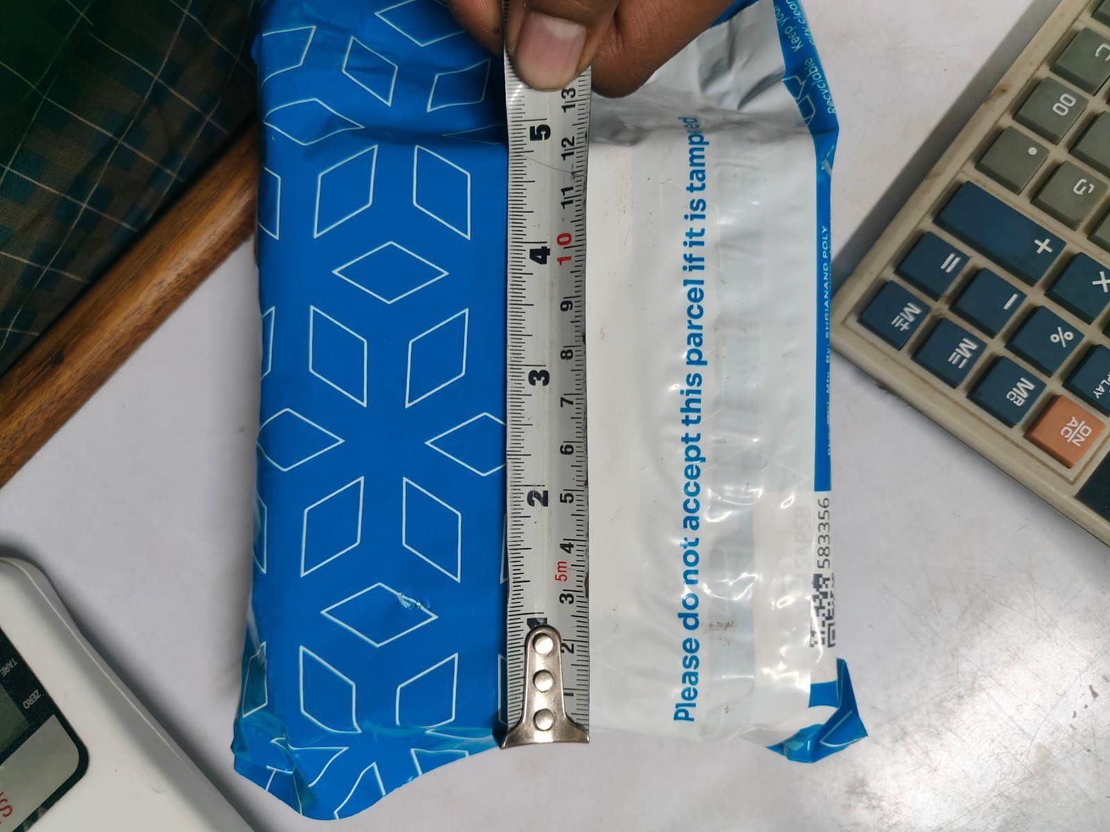 Blue package with a ruler for scale on a desk with a calculator and phone.