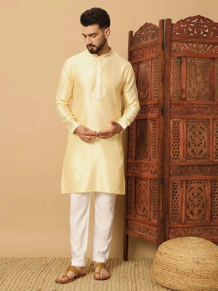 Man wearing a cream kurta with white pants standing next to a wooden carved screen.