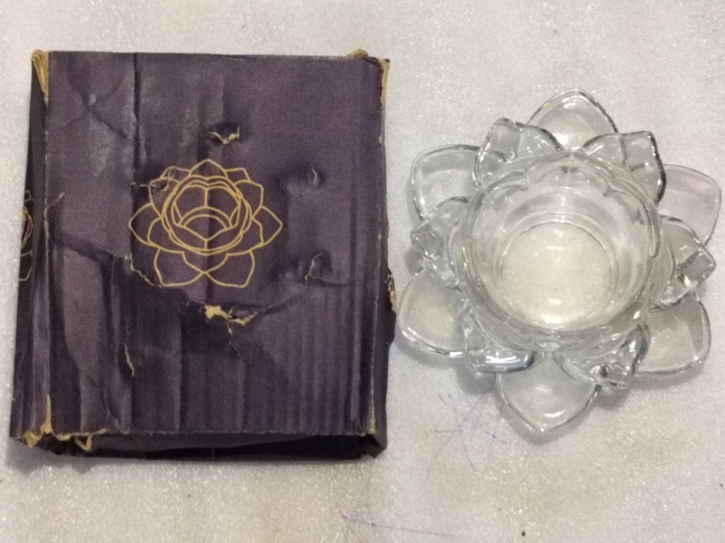Purple fabric with gold floral design and clear glass flower-shaped container on a light gray surface