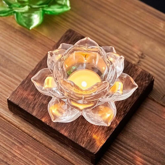 Clear glass lotus flower candle holder with a lit candle on a wooden base.